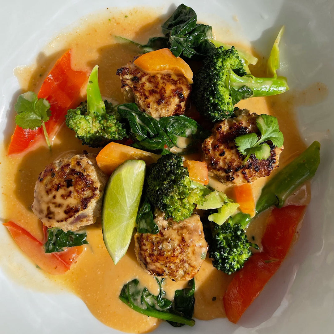 En tallrik med fyra kalkonbullar, paprika, broccoli och lime i röd currysås.