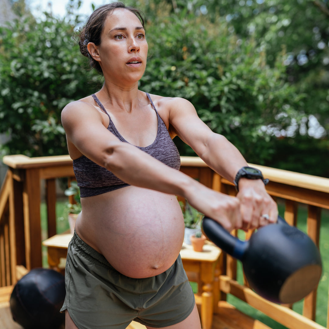 Gravid kvinna tränar kettlebell med fokus på kontroll och styrka.