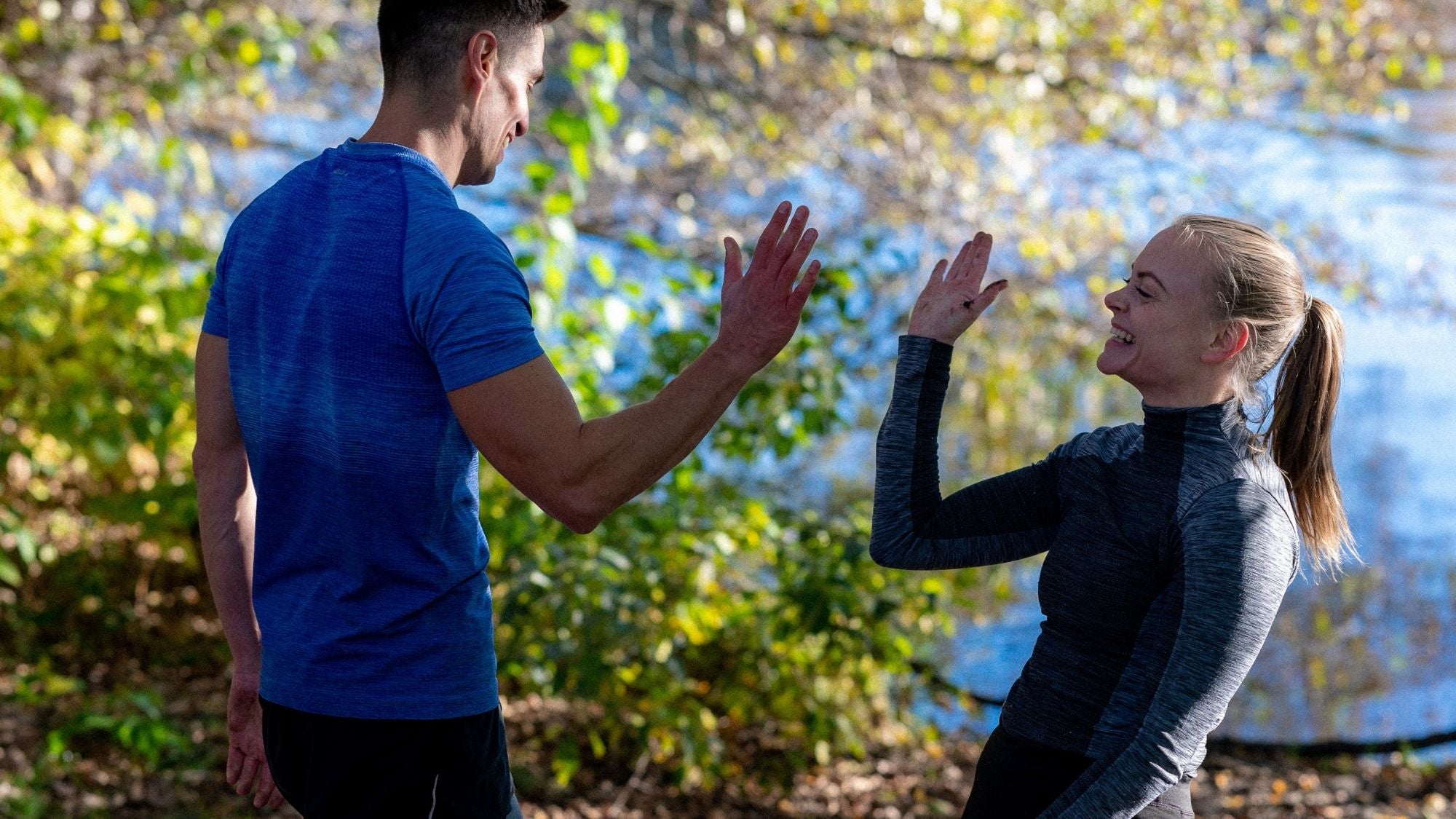 Kvinna och man gör high five efter träning med Bodily – kost och träningsprogram i naturen hemma och på gym