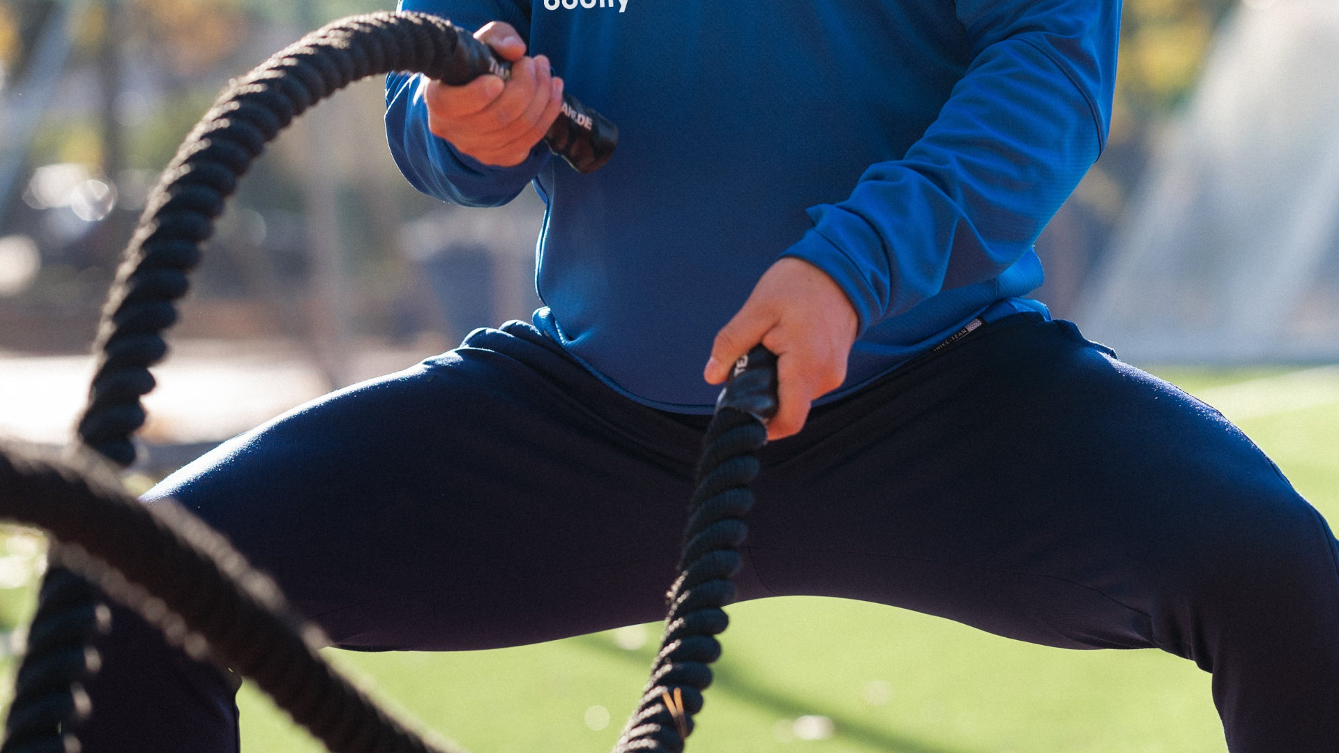 Deltagare tränar repslag med battle rope i HIIT-pass enligt Bodilys kost- och träningsprogram online.