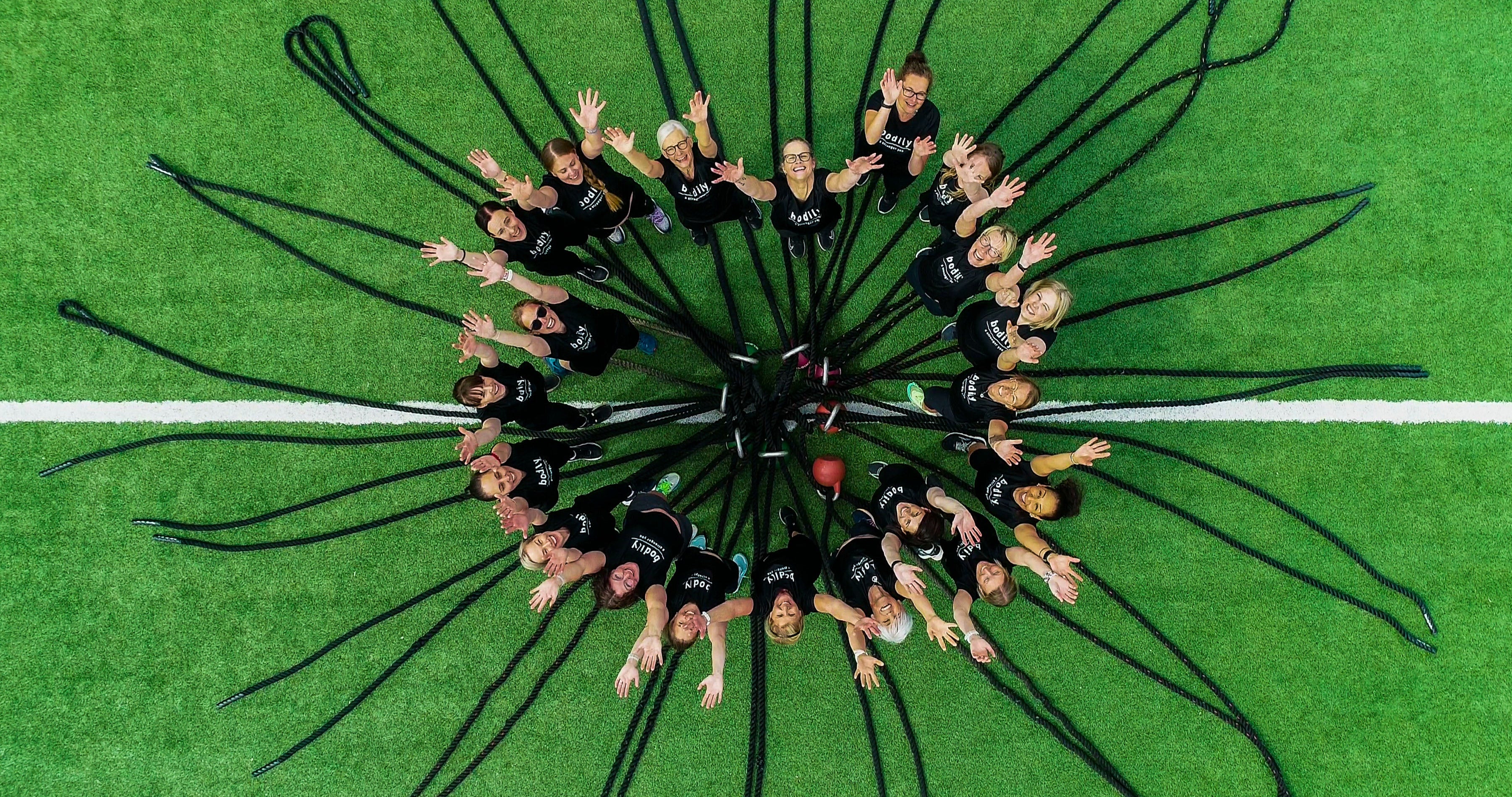 Hela Bodily-teamet står på grön konstgräsplan på Bosön med battle ropes – coacher, kostrådgivare och supportteam redo att coacha dig online